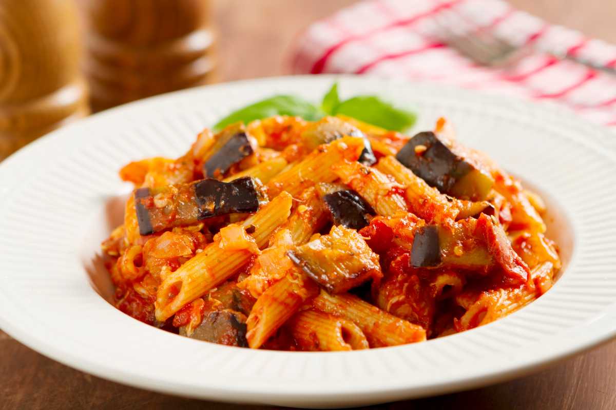 Piatto di pasta alla Norma e arancini su tavolo di legno